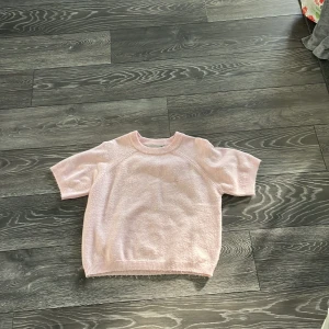 Ljusrosa stickad tröja 157/16 - Superfin ljusrosa stickad tröja med korta ärmar och rund hals. Mjuk och skön känsla, perfekt för dig som gillar en enkel men söt look. Ribbad kant vid hals, ärmslut och nederkant. Passar dig som vill ha en chill och feminin vibe.