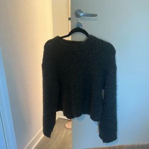 Mörkgrå stickad croppad tröja - Säljer en mörkgrå stickad tröja med croppad passform och ribbad struktur. Tröjan har rund hals och långa ärmar, perfekt för att hålla sig varm under kyliga dagar. Enkel och stilren design som funkar till många olika outfits.