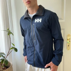Helly Hansen jacka  - Skön vindjacka perfekt för hösten. Inga större defekter förutom nära zipen så är det några minimala fläckar. Som du ser på sista bild! Kom med frågor! Modellen är 180,75 kg och bär M.