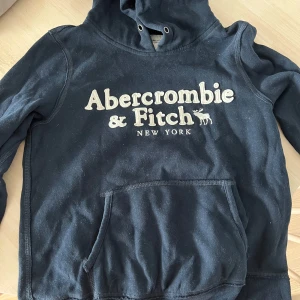 Mörkblå hoodie Abercrombie & Fitch - Säljer en mörkblå hoodie från Abercrombie & Fitch med stor vit logotyp på bröstet.