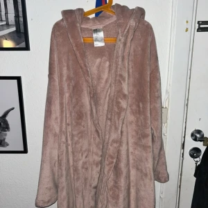 Rosa fleece morgonrock från H&M XS/S - Supermjuk och mysig beige/rosa fleece morgonrock från H&M i storlek XS/S. Har huva, långa ärmar och knyts med bälte i midjan. Perfekt för chill dagar hemma eller när du vill vara extra bekväm.