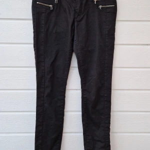 Svarta skinny jeans från ONLY, L - Svarta jeans från ONLY i skinny fit med snygga silverfärgade dragkedjor framtill. Klassisk femficksmodell med två bakfickor och knappstängning. Jeansen är tillverkade i bomull med lite stretch för skön passform. Fint skick. 