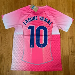 Barça Lamine Yamal Nike rosa matchtröja - Snygg FC Barcelona fotbollströja med Lamine Yamal och nummer 10 på ryggen. Tröjan är rosa med vita och blå detaljer. Nike-logga och Spotify som sponsor på bröstet. Perfekt för dig som vill sticka ut. 