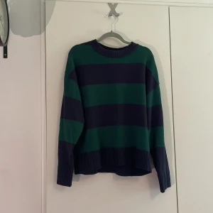Stickad tröja - Säljer en stickad tröja med breda mörkblå och gröna ränder. Tröjan har rund hals, långa ärmar och ribbade muddar vid ärmslut och nederkant. Perfekt för dig som gillar klassisk streetstyle med lite färg.