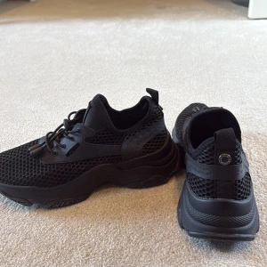 Svarta sneakers från Steve madden  - Säljer ett par svarta sneakers från Steve madden med chunky platt sula och mesh-överdel. Skorna har snörning med snabblås och detaljer i syntetmaterial. Snyggt sportig look med rund tå och coolt mönstrad mesh som ger extra edge.