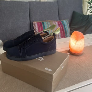 Mörkblå mocka sneakers Louboutin - Snygga mörkblå sneakers från Christian Louboutin i mjuk mocka med klassisk röd signatursula. Skorna har rund tå, platt sula och snörning. Perfekt för dig som vill ha en lyxig och stilren look med exklusiv känsla. Kommer med originalkartong och dustbag.
