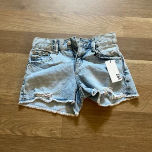 Ljusblå jeansshorts från 157 - Snygga ljusblå jeansshorts från 157 med fransig kant och slitna detaljer framtill. Klassisk femficksmodell med knapp och dragkedja. Perfekt för dig som gillar en chill och trendig stil på sommaren.