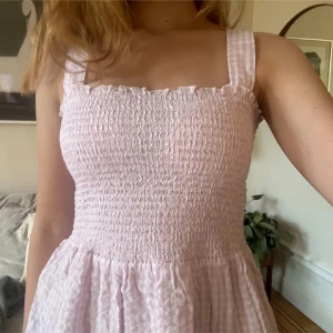 Ljusrosa smockad topp med breda axelband - Söt ljusrosa topp med smockad överdel och breda axelband. Toppen har ett subtilt rutigt mönster och är gjord i ett lätt, luftigt material som passar perfekt för varma dagar.