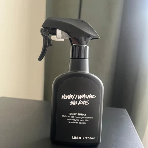 Honey I Washed The Kids Body Spray från Lush - Använd, där jag håller pennan visar hur mycket som används, mycket kvar !                                                        En svart sprayflaska med body spray från Lush i doften Honey I Washed The Kids. Doftar av söta honungskarameller med en syrlig twist från brasiliansk apelsin. Flaskan rymmer 200 ml och har en modern, stilren design.