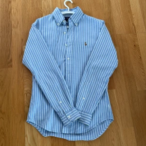Blåvit randig skjorta från Ralph Lauren - Säljer en blå skjorta med vita ränder från Ralph Lauren. Skjortan är i väldigt bra skick och har använt den endast 3 gånger. Säljer pågrund av att den inte passar mig. En riktigt stilig skjorta som passar helt perfekt till sommaren. Storlek S men passar även XS
