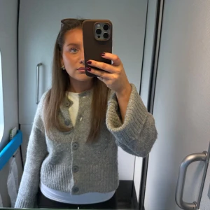 Grå kofta från Zara - Säljer en grå kofta från Zara med stora knappar framtill. Koftan är stickad och har långa ärmar samt ribbade muddar vid ärmslut och nederkant. Perfekt att slänga över en t-shirt eller linne.