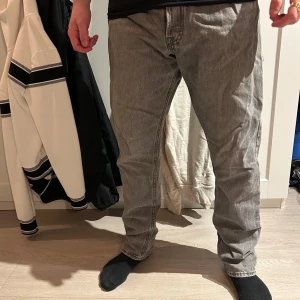 Grå jeansbyxor med rak passform - Säljer ett par grå jeansbyxor med klassisk femficksdesign och rak passform. Byxorna har normal midja och synliga sömmar längs benen. Perfekta för dig som gillar en enkel och stilren look.