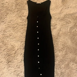 Svart ribbad klänning från Zara - Säljer svart känning från zara då den är lite stor på mig. Klänningen är lång och ribbad och man kan öppna de två översta knapparna. .