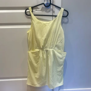 Ljusgul ärmlös omlottklänning - Söt ljusgul ärmlös klänning med omlottdetalj i ryggen och markerad midja. Klänningen har en kort längd och är perfekt för varma dagar. Enkel och stilren design som passar till många tillfällen.