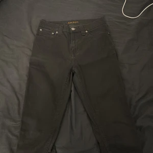Svarta jeans från Nudie Jeans - Säljer ett par svarta jeans från Nudie Jeans med klassisk femficksdesign och raka ben. Jeansen har normal passform. Perfekta för dig som gillar stilrena och tidlösa byxor.