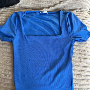 Blå topp med fyrkantig ringning från New yorker - Säljer en blå topp från New yorker med korta ärmar och snygg fyrkantig ringning. Toppens material känns mjukt och stretchigt. Säljer då den inte kommer till användning! 