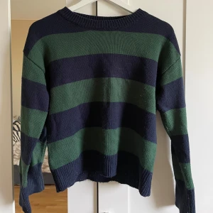 Randig stickad tröja i grönt och mörkblått - Säljer en stickad tröja med breda gröna och mörkblå ränder. Tröjan har rund halsringning, långa ärmar och ribbade muddar. Perfekt för kyligare dagar och enkel att styla till jeans eller kjol., så söt och skön!🩷