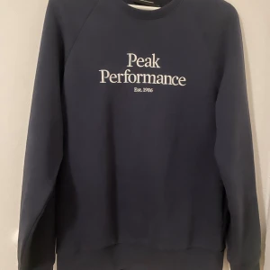 Mörkblå sweatshirt från Peak Performance - Mörkblå sweatshirt från Peak Performance med vit text på bröstet. Pris: 150kr