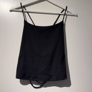 Svart croppad linnetopp med snörning - Säljer en svart croppad linnetopp med tunna axelband och snygg snörning i ryggen. Toppen har en enkel och stilren design framtill och korsade band baktill som ger en cool detalj.