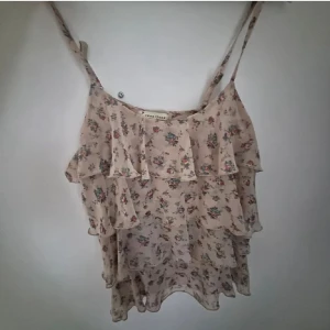 Blommig volangtop med smala axelband - Säljer en söt blommig topp från Vero Moda med volanger och smala axelband. Toppen är i en ljus beige färg med små blommor i rosa och grönt. Perfekt för varma dagar! skriv privat för fler frågor eller bilder, kan även gå ner i pris💞