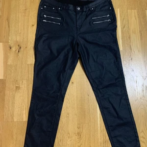 Svarta byxor med dragkedjedetaljer från VRS - Snygga svarta byxor från VRS med två dekorativa dragkedjor på varje sida framtill. Klassisk femficksmodell med normal passform och knappstängning. Perfekta för en trendig och stilren look.