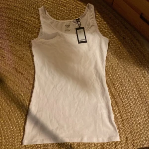 Vit linnetopp från 157 - Säljer en klassisk vit linnetopp från 157 i storlek XS. Toppen är ärmlös och har en rund halsringning. Tillverkad i mjuk bomull med lite elastan för extra stretch. Perfekt basplagg till garderoben!