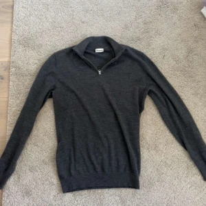 Mörkgrå halvzip tröja från John Henric  - Säljer en stilren mörkgrå tröja från John Henric med halv dragkedja vid halsen. Tröjan har lång ärm och ribbade muddar vid ärmslut och nederkant. Perfekt för lager-på-lager och snygg till både jeans och chinos.