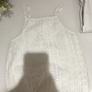 Vit spetslinne från Lindex Kids - Säljer ett vitt linne från Lindex Kids i storlek 134/140. Toppen har fina spetsdetaljer framtill och tunna axelband. Perfekt för varma dagar eller som ett lager under andra plagg.