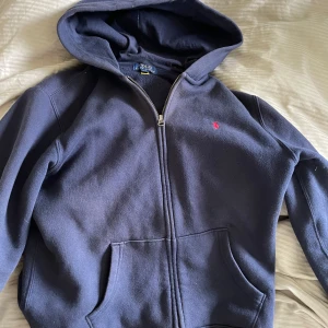 Mörkblå hoodie från Polo Ralph Lauren - Säljer min brorsas mörkblå hoodie från Polo Ralph Lauren med dragkedja och huva. Det är L i junior storlek så skulle säga att den är som xs/s