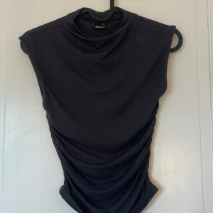 Svart ärmlös topp från Gina Tricot - Säljer en mörkgrå ärmlös topp från Gina Tricot. Toppen har en enkel och stilren design med rund halsringning och mjukt material. Perfekt att matcha med jeans eller kjol för en snygg look. Perfekt till sommaren. Säljer för den inte används 