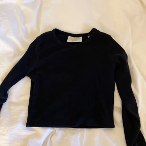 Svart ribbad croppad tröja - Säljer en svart ribbad croppad tröja med lång ärm i storlek S. Tröjan har en enkel och stilren design, perfekt att matcha med jeans eller kjol. Tillverkad i ett mjukt och stretchigt material för en bekväm passform.