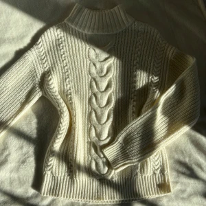 Vit stickad polotröja från Vila - Säljer en vit stickad polotröja från Vila med grov kabelstickning framtill och ribbade muddar. Tröjan har lång ärm och hög polokrage, perfekt för kyliga dagar eller sommarkvällar över en klänning! 