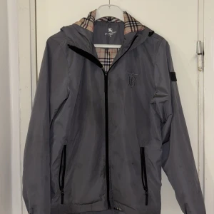Grå vindjacka från Burberry - Uppgradera din vårstil med denna exklusiva Burberry-jacka – en perfekt kombination av lyx och funktion.