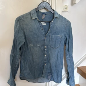 Jeansskjorta från G-Star RAW - Snygg ljusblå jeansskjorta från G-Star RAW med klassisk krage och bröstficka. Skjortan har knappar framtill och är långärmad. Perfekt för dig som gillar en avslappnad men stilren look.