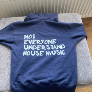 Blå hoodie med tryck från Hopily - Säljer en blå hoodie från Hopily i storlek XS. Tröjan har huva med dragsko, magficka och ett stort vitt tryck på ryggen med texten 'Not everyone understand house music'. Perfekt för dig som gillar streetwear.