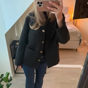 Svart kavaj med guldknappar - Stilren svart kavaj med guldknappar framtill och två stora fickor. Klassisk rak passform och lång ärm. Perfekt att styla till jeans eller kjol för en snygg look.