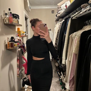 Svart långklänning med slits och cut-out - Säljer en svart långklänning med lång ärm, hög hals och snygg cut-out vid midjan. Klänningen har en slits framtill som ger en extra touch. Perfekt för dig som vill ha en stilren och trendig look. Passar både m och s.