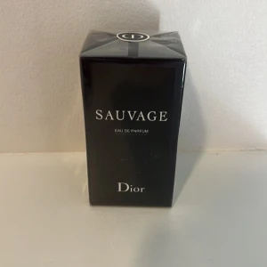 Sauvage Eau de Parfum från Dior 60ML - Sauvage Eau de Parfum från Dior i elegant svart kartong med silverdetaljer. Parfymen är känd för sin fräscha och kryddiga doftprofil. Förpackningen har tydlig Dior-logga på toppen och stilren design. PRIS KAN DISKUTERAS 