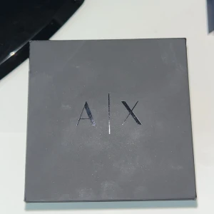 Armani Exchange herrklocka i silver - Stilren herrklocka från Armani Exchange med svart urtavla och datumvisning. Klockan har ett klassiskt armband i silverfärgad metall och tydliga vita markeringar på urtavlan. Perfekt accessoar för dig som gillar en modern och elegant look.