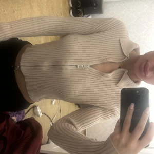 Beige ribbad kofta med dragkedja - Säljer en beige ribbad kofta med dragkedja framtill. Tröjan har lång ärm samt krage. 