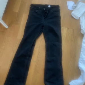 Svarta bootcut jeans - Säljer ett par svarta bootcut jeans med klassisk femficksdesign och knappgylf. Jeansen har en något utsvängd passform nertill och är perfekta för dig som gillar en tidlös stil.