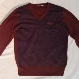 Vinröd stickad tröja  - Säljer en stickad tröja från Armani Jeans. Tröjan har v-ringning och broderad AJ-logga på bröstet. Bra kondition använd en gång eller två, storlek medium. 