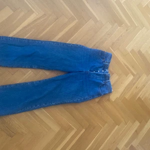 Levi's Ribcage Straight jeans blå - Säljer ett par klassiska blå Levi's Ribcage Straight jeans med hög midja och raka ben. Jeansen har fem fickor, knäppning med knappar och är tillverkade i slitstarkt denim. Perfekta för en tidlös och avslappnad look. Frakt tillkommer
