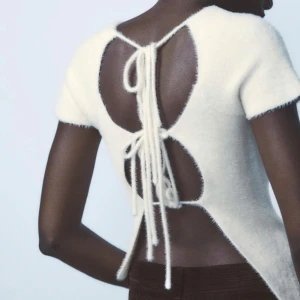 Vit stickad topp med snörning - Säljer en stilren vit stickad topp med korta ärmar och snygg snörning i ryggen.