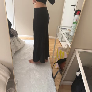 Svart långkjol med utsvängd passform - Säljer en svart långkjol med utsvängd siluett. Kjolen har en hög midja och är i ett mjukt, följsamt material som ger en snygg och bekväm look. Perfekt att styla med crop tops eller stickade tröjor.