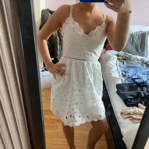 Vit spetsklänning - Säljer en söt vit klänning med smala axelband och v-ringning. Klänningen har vackra broderade blommor i spets. Perfekt för sommarens alla tillfällen!