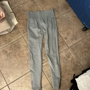 Grå höga leggings med ribbade detaljer - Snygga ljusgrå leggings med hög midja och ribbade detaljer längs sidorna. Tillverkade i stretchigt material med 90% polyamid och 10% elastan för en tight och bekväm passform. Perfekta för träning eller chill dagar.