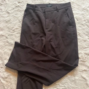 Bruna kostymbyxor från Lindex - Snygga bruna kostymbyxor från Lindex, modell Fiona. (Midwaisted) Klassisk rak passform med hällor för bälte och diskreta fickor. Storlek 38🩷