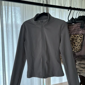 Beige yoga jacka med dragkedja H&M move - Säljer en stilren beige jacka från H&M med hög krage och hel dragkedja framtill. Jackan har lång ärm och minimalistisk design, perfekt för dig som gillar en clean look.
