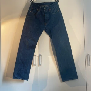 Levi's 501 jeans blå W32 L30 - Klassiska blå Levi's 501 jeans med raka ben och normal passform. Byxorna har fem fickor, knappar i gylfen och tydliga Levi's-detaljer som röd etikett och läderpatch bak. Perfekta för dig som gillar tidlös denimstil.